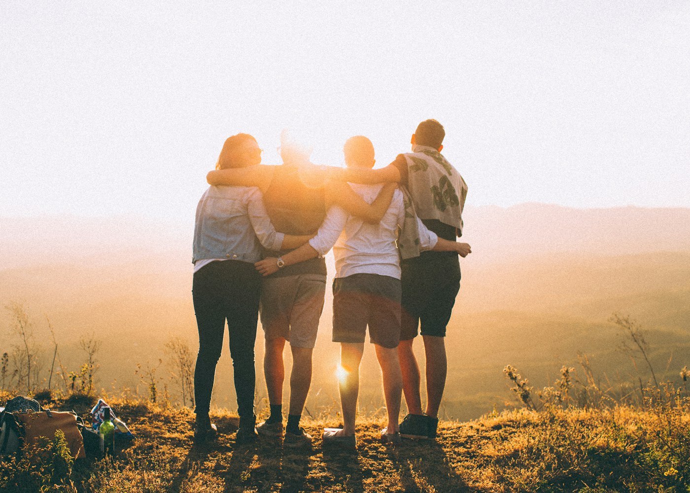 Four people with arms around one another looking out at a sunset