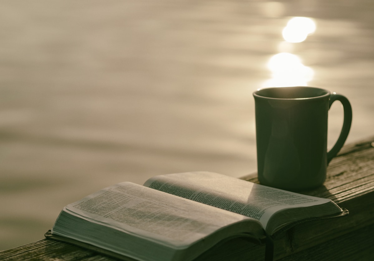An open Bible on a table beside a mug of coffee in morning light