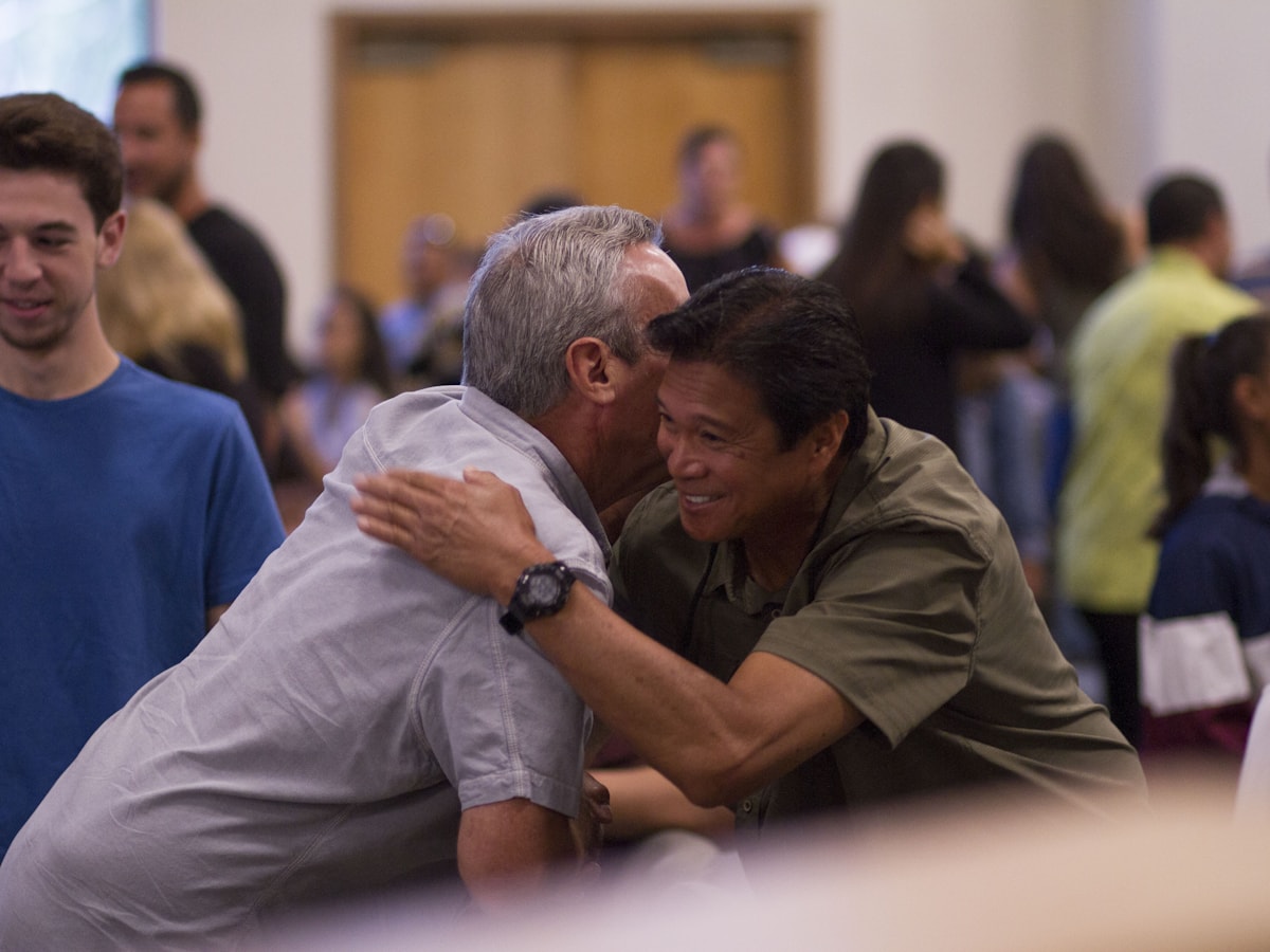 Two men greeting each other with a hug in a church lobby
