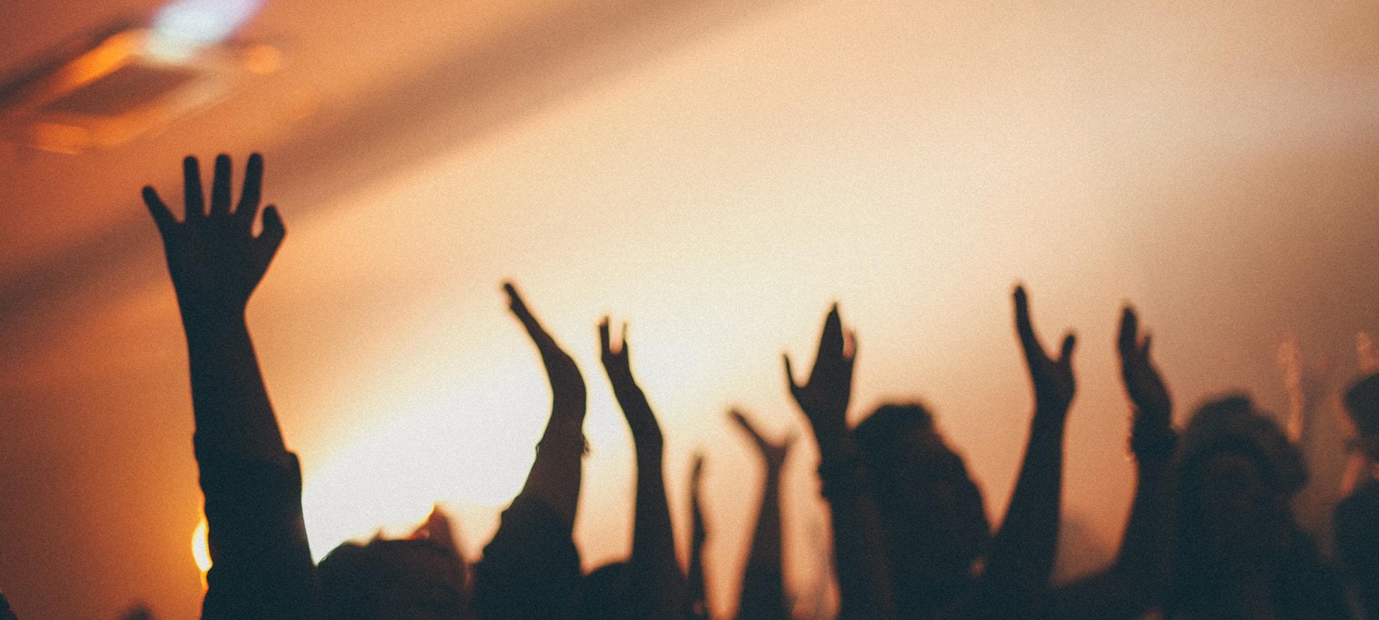 Silhouettes of a congregation with arms raised in worship at sunset